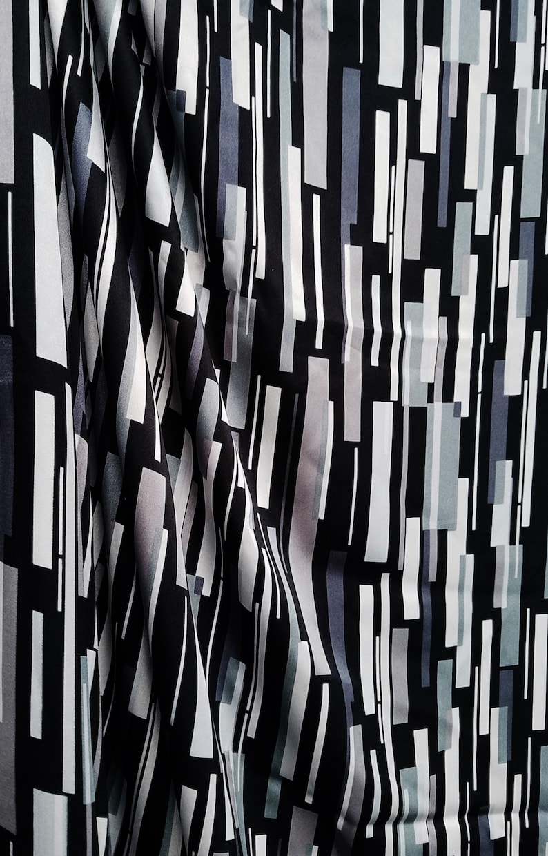 May include: Black and white fabric with a geometric pattern of vertical and horizontal lines and rectangles. The fabric has a subtle sheen and a smooth texture.