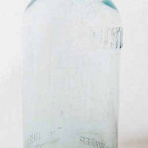 May include: A clear glass bottle with a cork stopper. The bottle is labeled "Pure Distilled Water" and "The Distilled Water Co."