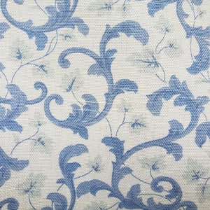 Dekorationstyg från 5th Avenue Designs för Covington. Krämfärgad bakgrund med blå rullar och ljusgröna löv. Draperitjocklek