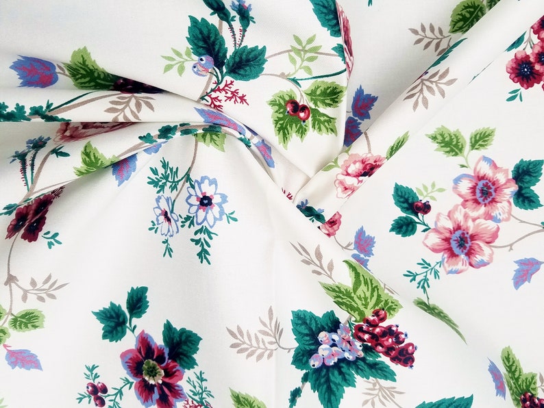 May include: White fabric with a floral pattern featuring pink, red, blue, and green flowers. The fabric has a subtle sheen and a soft texture.