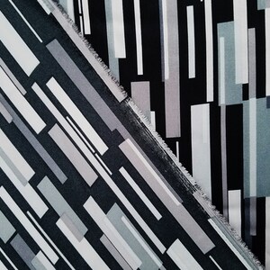 May include: Two pieces of fabric with a geometric pattern of black, white, and gray stripes. The fabric is cut at a diagonal angle.