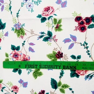 May include: White fabric with a repeating floral pattern. The pattern features pink, red, and blue flowers with green leaves. A green ruler with the text "FIRST SECURITY BANK" is placed across the fabric.