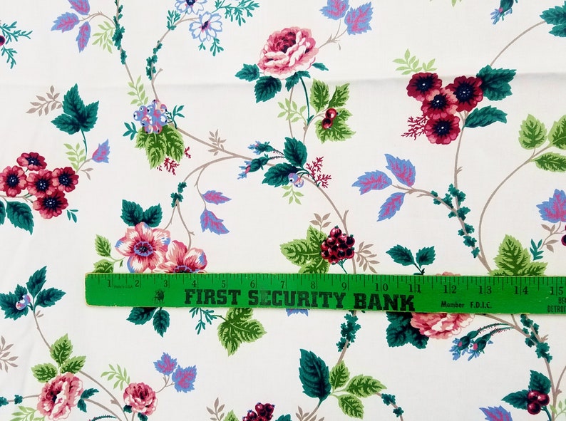 May include: White fabric with a repeating floral pattern. The pattern features pink, red, and blue flowers with green leaves. A green ruler with the text "FIRST SECURITY BANK" is placed across the fabric.