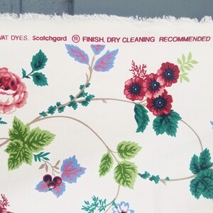 May include: White cotton fabric with a floral pattern featuring pink, red, and blue flowers. The fabric has a label that reads "VAT DYES. Scotchgard&reg; FINISH. DRY CLEANING RECOMMENDED."
