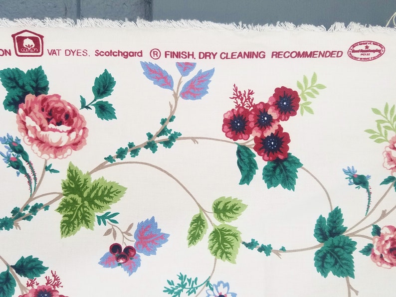 May include: White cotton fabric with a floral pattern featuring pink, red, and blue flowers. The fabric has a label that reads "VAT DYES. Scotchgard&reg; FINISH. DRY CLEANING RECOMMENDED."
