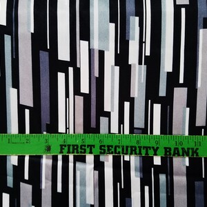May include: Black fabric with a geometric pattern of white, gray, and light blue rectangles. A green ruler with the text "FIRST SECURITY BANK" is placed on top of the fabric.