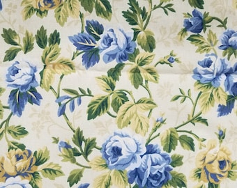 May include: A white fabric with a floral pattern featuring blue and yellow roses with green leaves.