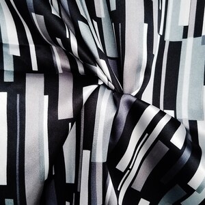 May include: Black and white striped fabric with a geometric pattern. The fabric is made of a silky material and has a smooth texture.