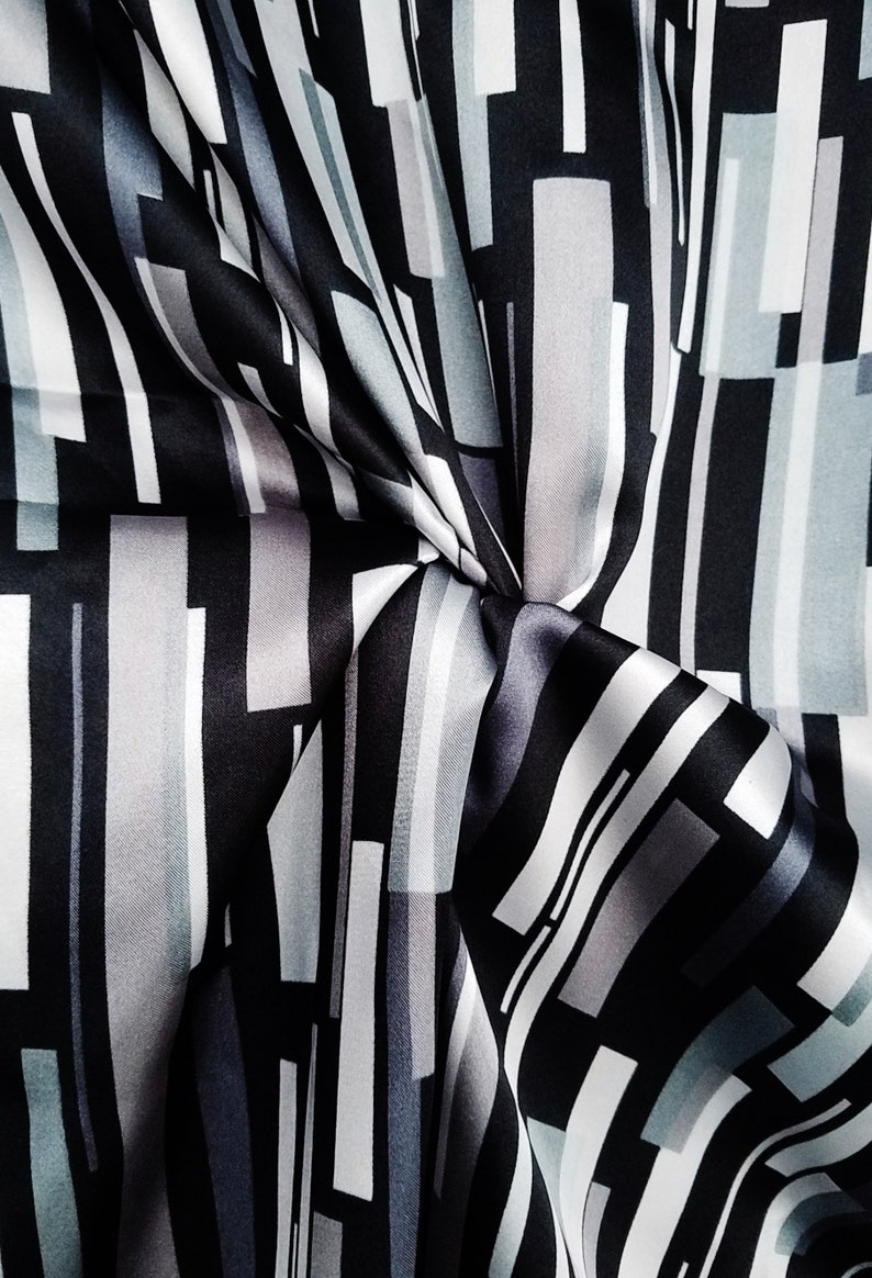 May include: Black and white striped fabric with a geometric pattern. The fabric is made of a silky material and has a smooth texture.