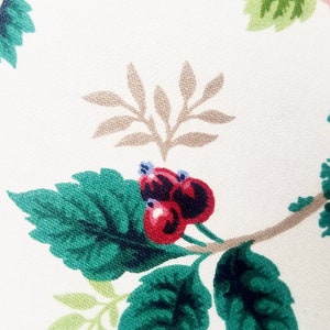 May include: A close-up of a fabric with a floral pattern. The pattern features green leaves, brown branches, and red berries.