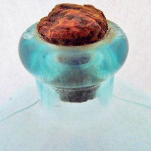 May include: A vintage glass bottle with a blue tint and a rusty cork stopper. The bottle has a rounded body and a narrow neck.