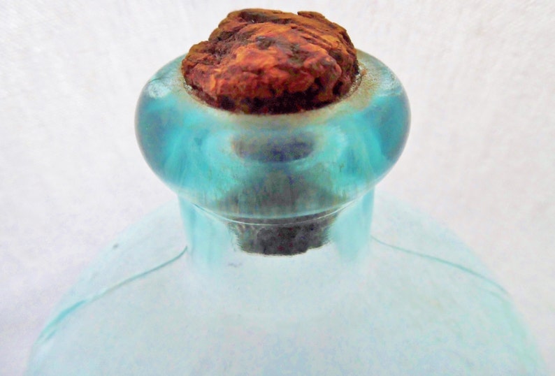 May include: A vintage glass bottle with a blue tint and a rusty cork stopper. The bottle has a rounded body and a narrow neck.