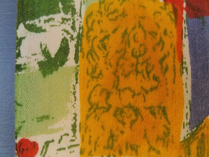 Pu&ograve; includere: Primo piano di un tessuto con un motivo astratto colorato. Il tessuto presenta una grande sezione gialla con scarabocchi verdi, una sezione verde con forme bianche e una sezione rossa e blu.