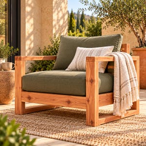 May include: A wooden armchair with a natural light brown finish, featuring thick olive green seat and back cushions. A small rectangular cream-coloured throw pillow with thin brown stripes and a cream-coloured knit throw blanket with tassels.