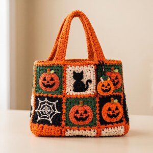 May include: A handmade crochet tote bag featuring a patchwork design of Halloween-themed squares. The bag displays orange pumpkins, a black cat, and a white spiderweb on black, green, and white backgrounds. It includes two orange handles and a pumpkin charm.