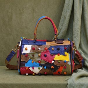 May include: A multi-colored leather handbag featuring a patchwork design of various shapes and textures. The bag includes two top handles, a detachable shoulder strap, and small, raised, colorful circular studs scattered across the surface.