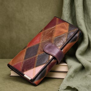 May include: A rectangular leather wallet featuring a patchwork design of diamond-shaped panels in shades of burgundy, brown, tan, and light pink. The panels are joined by visible zigzag stitching, and the wallet includes a snap-button closure.