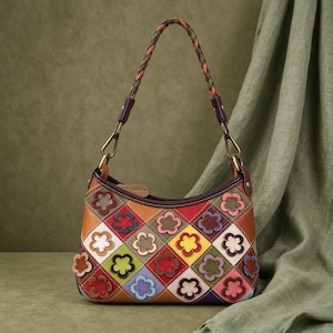 May include: A multi-colored handbag featuring a diamond-patterned exterior with various leather patches in shades of red, yellow, green, blue, and brown. Each diamond contains a small, layered flower appliqué. It has a braided leather handle.