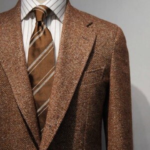 May include: A brown herringbone blazer with a white and brown striped dress shirt and a brown striped necktie. The Milano Stitch logo is visible in the upper right corner, featuring the letters MS inside a gold laurel wreath design.
