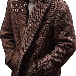 May include: A brown herringbone coat with a textured finish and subtle multi-colored flecks, featuring a notched lapel and side pockets. The text MILANO STITCH is visible in the upper left corner over a circular logo with the letters MS.