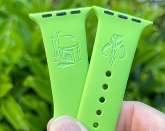 May include: Two green Apple Watch bands with embossed Star Wars characters. One band features Boba Fett's helmet and the other features a Mandalorian symbol.