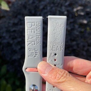 May include: Two gray silicone watch bands with the text "Brother Bear" and a bear graphic.