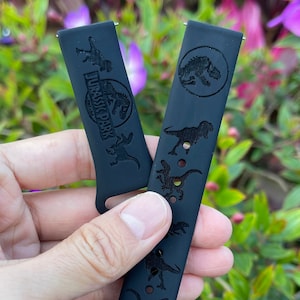 May include: Black silicone watch band featuring a Jurassic Park logo and dinosaur silhouettes.