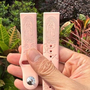 May include: Two pink silicone watch bands with a raised design of the Virgin Mary, roses, and a rosary.