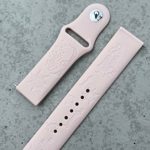 Puede incluir: Una pulsera de reloj de silicona rosa con un diseño blanco con personajes y símbolos de la película de Disney Tangled. La pulsera tiene el texto "I see the light" y "Tangled" impreso en ella.