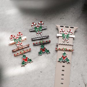 May include: A set of Christmas-themed watch band charms featuring candy canes, holly leaves, and a Mickey Mouse head. The charms are made of metal and have red, green, and white enamel. The charms are designed to be attached to a watch band.