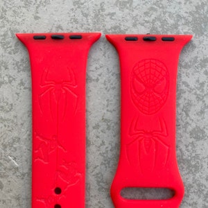 May include: Two red silicone Apple Watch bands with a Spiderman design. One band features a Spiderman head and the other features a Spiderman silhouette.