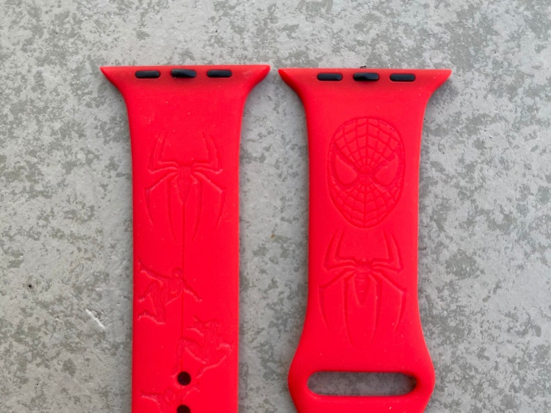 May include: Two red silicone Apple Watch bands with a Spiderman design. One band features a Spiderman head and the other features a Spiderman silhouette.