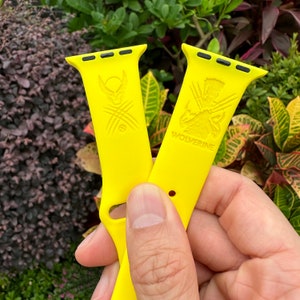 May include: Two yellow Apple Watch bands with black accents. One band features a Wolverine graphic and the word "Wolverine". The other band features a graphic of Wolverine's claws.