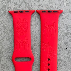 May include: A pair of bright red Apple Watch bands with a Spiderman design. The bands have a black top with three holes for the watch band.