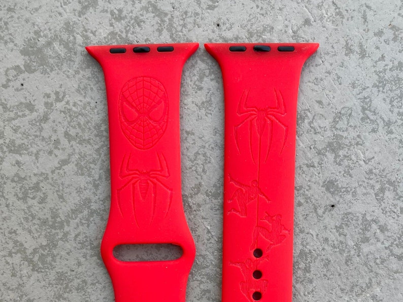May include: A pair of bright red Apple Watch bands with a Spiderman design. The bands have a black top with three holes for the watch band.