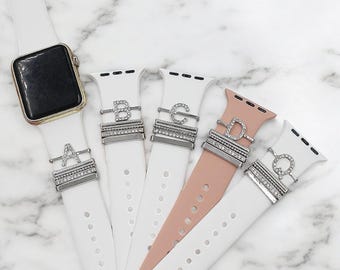 May include: Five different Apple Watch bands with interchangeable charms featuring the letters A, B, C, D, and Q. The charms are made of silver metal and have clear rhinestones.