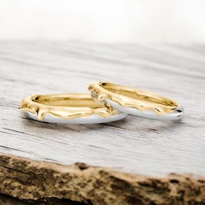 May include: Two gold wedding bands with a white gold base. The gold is dripping down the sides of the bands, creating a unique and modern look.