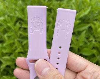 Op de afbeelding: Twee lavendelkleurige siliconen horlogebandjes met verschillende reliëfdesigns. Het bandje aan de linkerkant heeft een robotontwerp en het bandje aan de rechterkant heeft een gestileerd gezichtsontwerp.