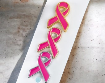 May include: Three pink ribbon pins with gold accents. The ribbons are in a stacked formation, with the top ribbon slightly offset to the right.