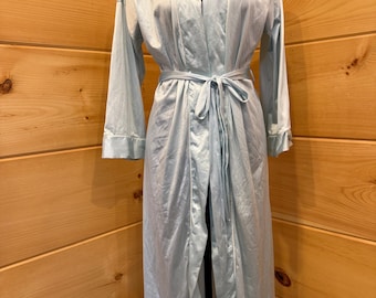 May include: A light blue, long-sleeved robe with a smooth, satin-like finish. The garment features a shawl collar with white piping trim, long sleeves with cuffs, and a matching fabric tie belt at the waist to secure the front closure.