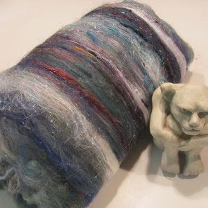 May include: A roll of colorful, sparkly yarn with iridescent fibers. The yarn is a mix of blues, purples, pinks, and whites.