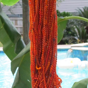 May include: A skein of hand-spun art yarn in vibrant shades of orange, red, and yellow, featuring a highly textured, twisted ply construction with small, colorful flecks and occasional metallic accents integrated throughout the fiber strands.