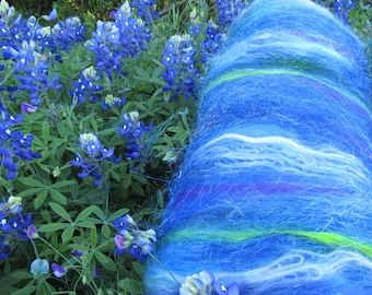 May include: A skein of blue, white, and green hand-spun yarn with a fuzzy texture. The yarn is arranged in a spiral shape and is sitting on a bed of blue flowers.
