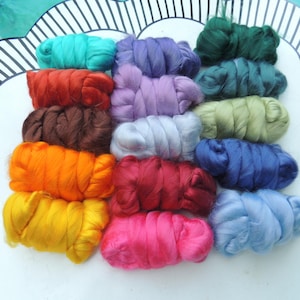 May include: A collection of colorful fiber bundles in shades of teal, purple, green, red, brown, orange, yellow, pink, and blue. The fibers are arranged on a white surface with a decorative border, ideal for crafting projects.