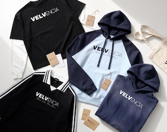 May include: A collection of apparel including a black long-sleeve layered t-shirt, a navy and light blue raglan hoodie, a black collared shirt with white stripes, and a solid navy hoodie, all featuring the Velvencia brand logo and tags.