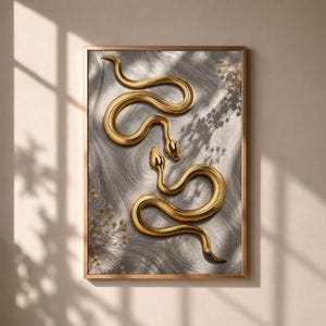 May include: A framed wall art print featuring two metallic gold snakes intertwined against a textured grey background with soft, blurred shadows of foliage cast across the surface, enclosed in a thin, matching gold-toned rectangular frame.