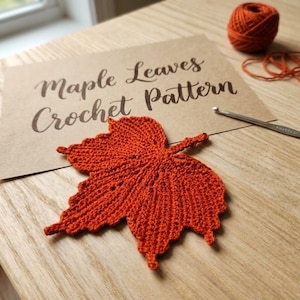 May include: A burnt orange crocheted maple leaf next to a ball of matching yarn and a metal crochet hook. A tan card features the text Maple Leaves Crochet Pattern in dark brown script, providing instructions for this detailed leaf design.