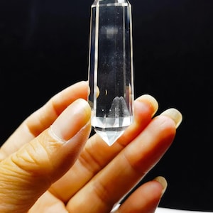 May include: A clear, transparent, double-terminated quartz crystal point with a hexagonal shape and smooth, polished facets. The crystal is colorless and features a sharp, pointed tip at both ends, showcasing internal clarity and light refraction.