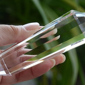 May include: A clear, transparent, double-terminated quartz crystal point with a smooth, polished, multi-faceted surface. The elongated, hexagonal-shaped crystal features sharp, pointed ends on both sides, reflecting light through its body.