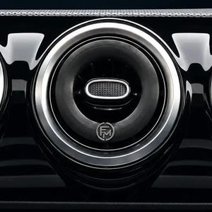 Könnte beinhalten: Ein Auto-Armaturenbrett mit drei runden Lüftungsdüsen mit silberner Metallverkleidung und schwarzen Lamellen. Unter den Lüftungsdüsen befindet sich ein zentrales Bedienfeld mit Tasten und Symbolen für die Klimaeinstellungen auf einer glänzend schwarzen Oberfläche.